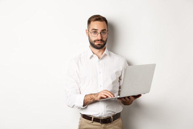 Negocio. Joven empresario guapo trabajando en equipo portátil, haciendo trabajo en equipo, de pie