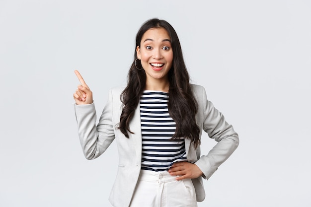 Negocios, finanzas y empleo, concepto de mujeres emprendedoras exitosas. Alegre empresaria exitosa en traje blanco apuntando con el dedo en la esquina superior izquierda, mostrando publicidad.