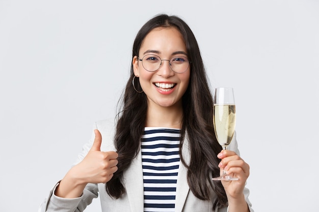 Negocios, finanzas y empleo, concepto de mujeres emprendedoras exitosas. Feliz empresaria asiática celebrando, celebrando una fiesta en la oficina, bebiendo champán y mostrando el pulgar hacia arriba