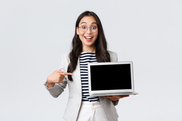 Negocios, finanzas y empleo, concepto de mujeres emprendedoras exitosas. Gerente de oficina entusiasta mostrando su presentación en la computadora portátil, apuntando a la pantalla y sonriendo divertido.