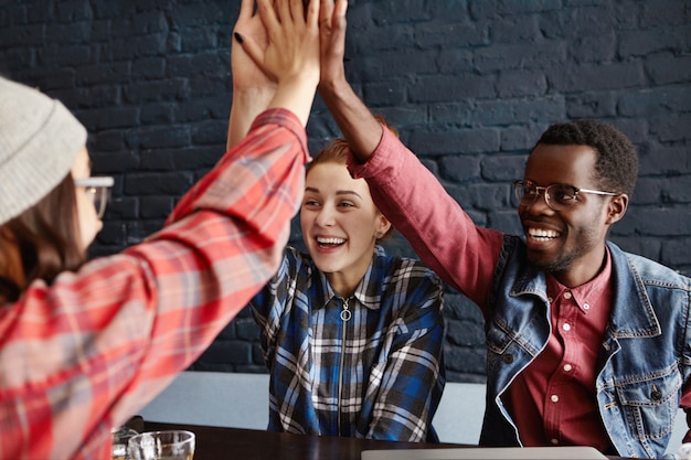 Negocios, puesta en marcha y trabajo en equipo. Equipo creativo feliz y entusiasta de emprendedores en ropa informal que se dan cinco entre sí, celebrando el éxito en el café