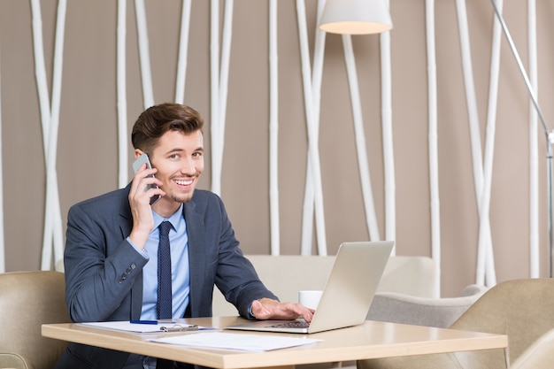 De negocios que trabaja en la computadora portátil y hablando por teléfono