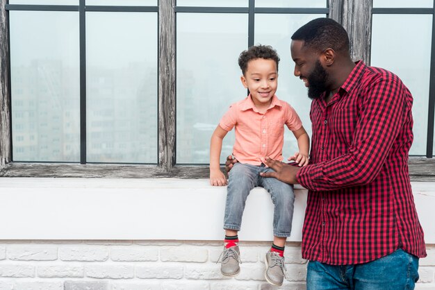 Negro padre e hijo hablando en el alféizar de la ventana