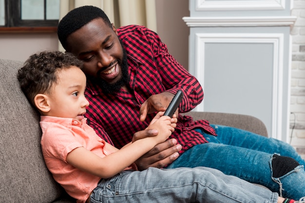 Negro padre e hijo usando teléfono inteligente en el sofá