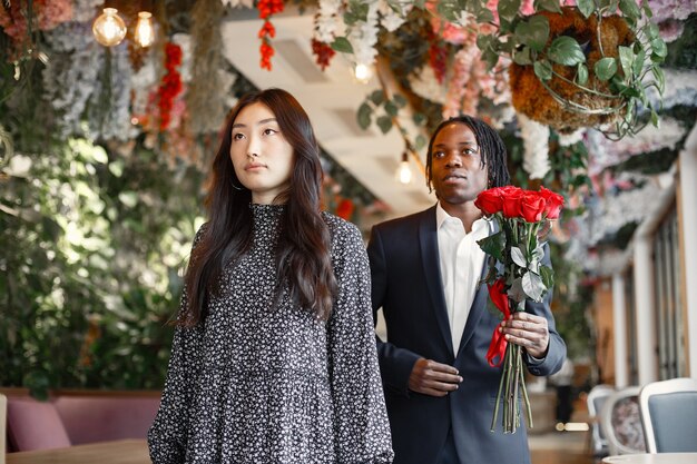 Negro con rastas. Chica con un vestido de fiesta. Ramo de rosas rojas.