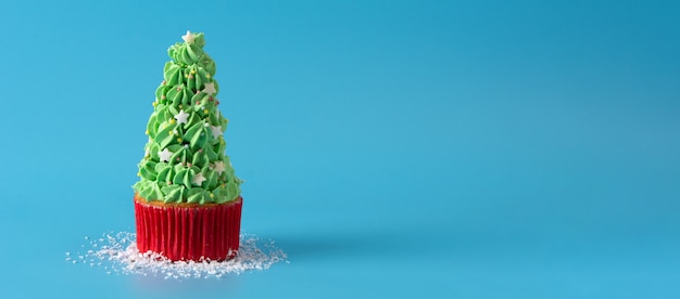 Nevando en cupcakes de árbol de Navidad aislado sobre fondo azul.