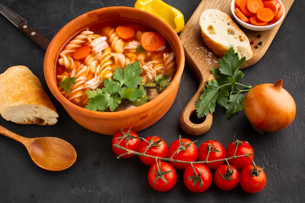 Ángulo alto brócoli zanahorias y fusilli en un tazón con pan en la tabla de cortar y cuchara de madera