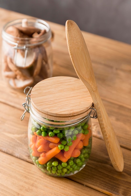 Ángulo alto de guisantes y zanahorias pequeñas en un frasco de vidrio con cuchara