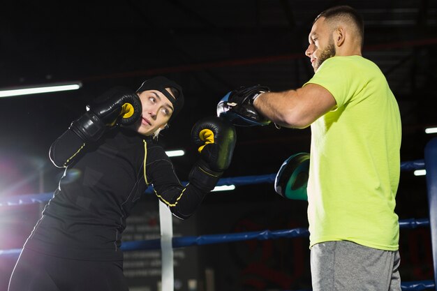 Ángulo bajo de boxeadora practicando con un entrenador masculino en el ring