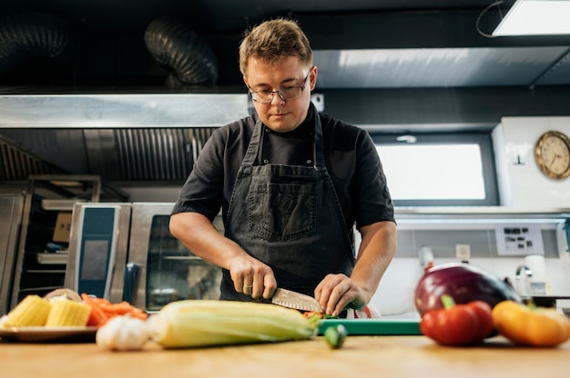 Ángulo bajo de chef masculino para picar verduras en la cocina