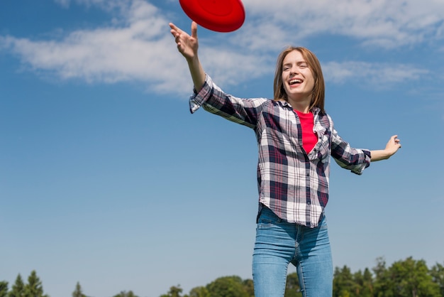 Ángulo bajo chica rubia jugando con un frisbee rojo