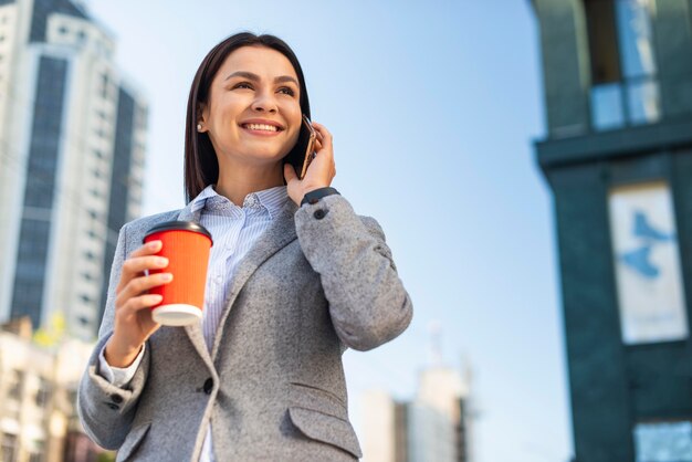 Ángulo bajo de empresaria sonriente hablando por teléfono mientras toma café