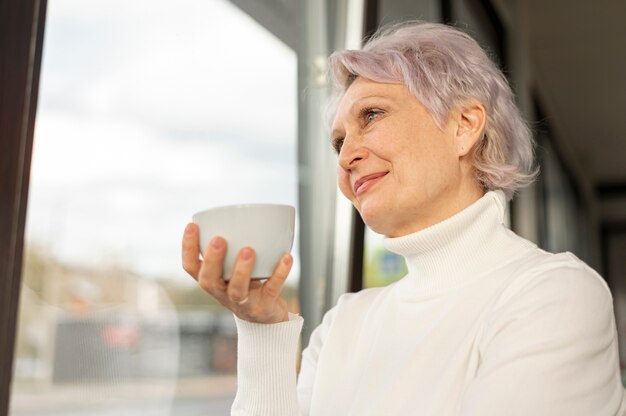 Ángulo bajo hembra con taza de café mirando por la ventana