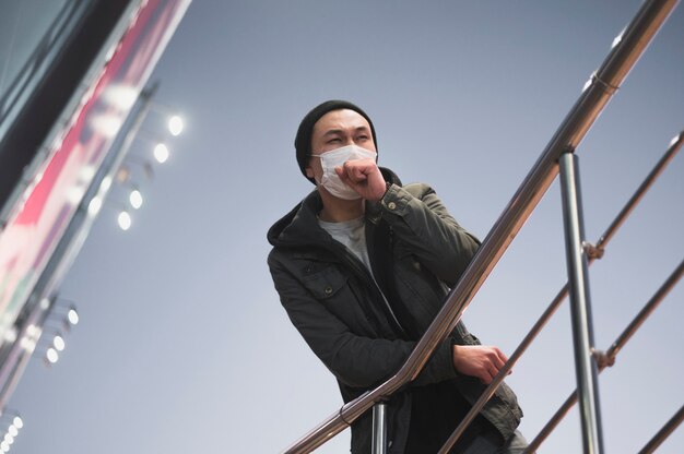 Ángulo bajo del hombre tosiendo mientras usa una máscara médica