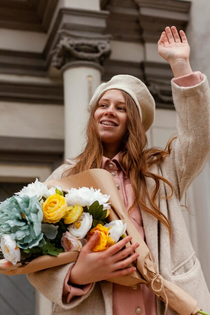 Ángulo bajo de mujer elegante al aire libre con ramo de flores en la primavera