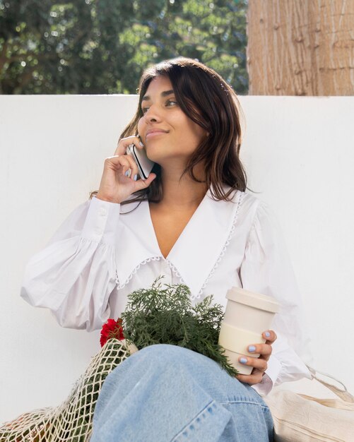 Ángulo bajo de mujer hablando por teléfono al aire libre mientras toma un café