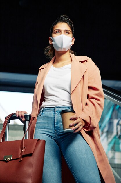 Ángulo bajo de mujer con máscara médica y equipaje en el aeropuerto