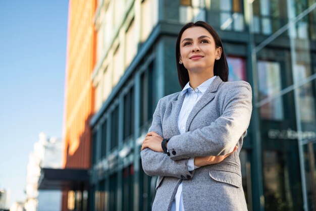 Ángulo bajo, de, mujer de negocios, posar, con, armamentos cruzaron, aire libre