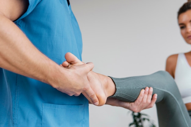 Ángulo bajo del terapeuta osteopático masculino que controla el movimiento de la pierna del paciente femenino