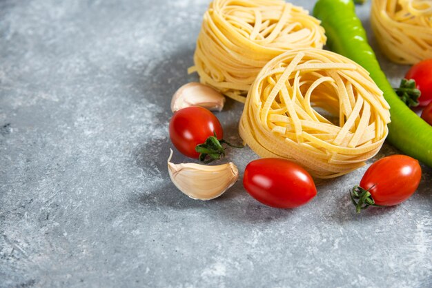 Nido de espaguetis crudos con verduras sobre un fondo de mármol