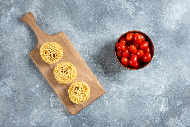 Nido de pasta sobre tabla de madera con plato de tomates.