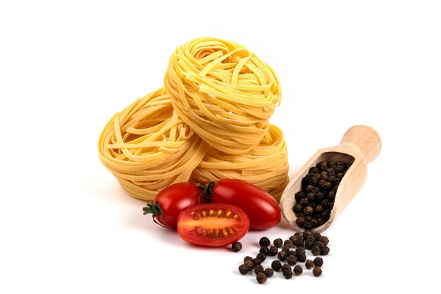 Nidos de espaguetis crudos, tomates y granos de pepepr en blanco.