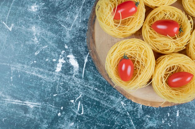 Nidos de espaguetis crudos con tomates sobre tabla de madera.