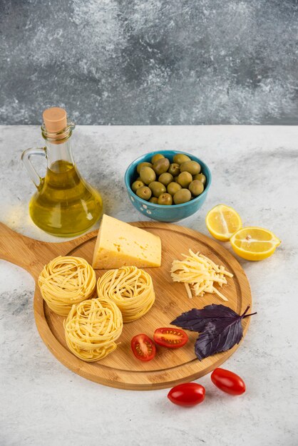 Nidos de espaguetis, verduras y queso sobre tabla de madera con aceitunas.
