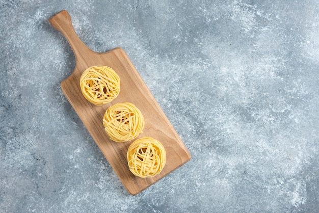 Nidos de pasta cruda sobre tabla de madera.