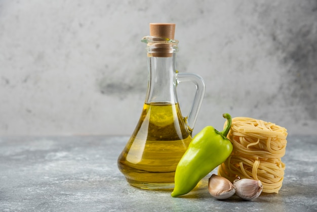 Nidos de pasta cruda de tagliatelle, botella de aceite y verduras sobre fondo de mármol.