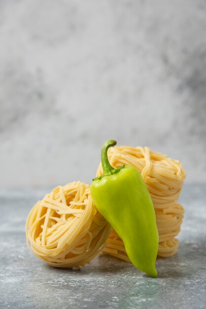 Nidos de pasta cruda de tallarines y pimiento verde sobre mesa de mármol.