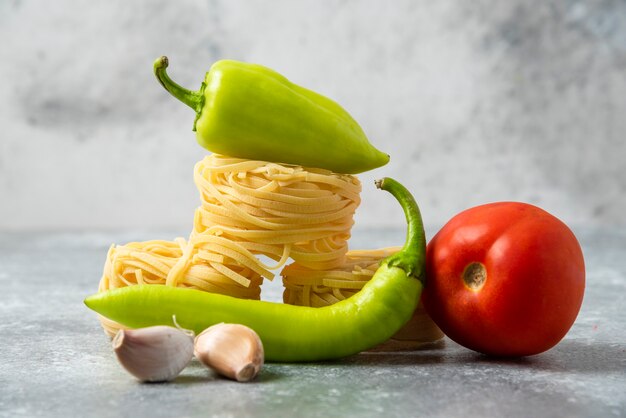 Nidos de pasta cruda de tallarines y verduras en la mesa de mármol.