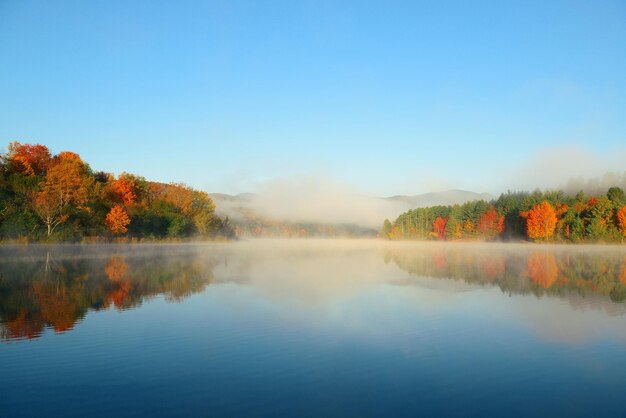 Niebla del lago con follaje otoñal y montañas con reflejo en New England Stowe