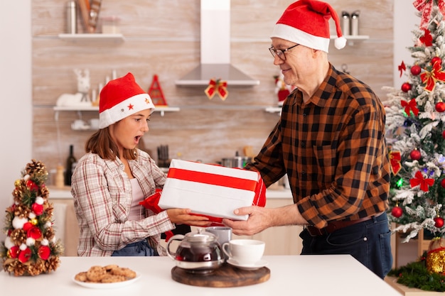 Nieta abuelo sorprendente con regalo de envoltura celebrando la fiesta de navidad