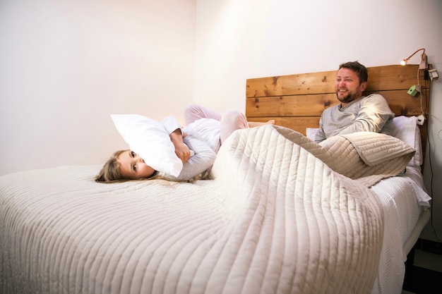 Foto gratuita niña abrazando una almohada en la cama junto a su padre