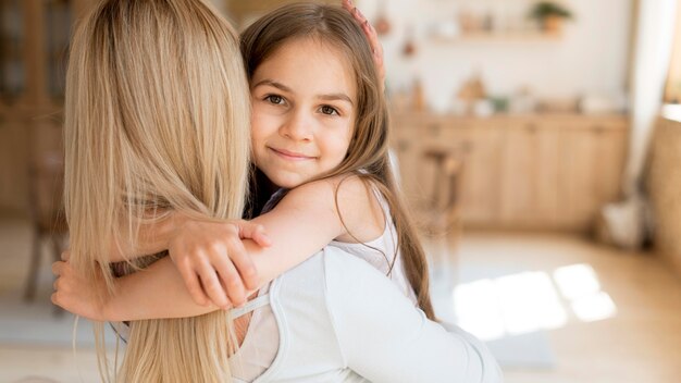 Niña abrazando a su madre mientras está en casa