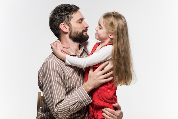 Niña abrazando a su padre sobre una pared blanca