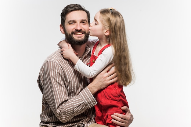 Niña abrazando a su padre sobre una pared blanca