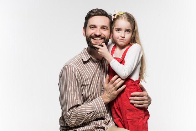 Niña abrazando a su padre sobre una pared blanca