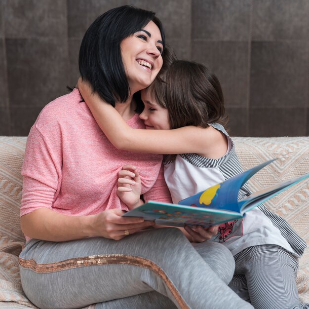 Niña, abrazar, madre, con, libro, en, sofá