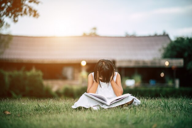 Niña aburrida leyendo en el jardín de la casa