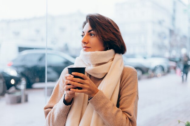 Una niña en un acogedor café se calienta con una taza de café caliente.