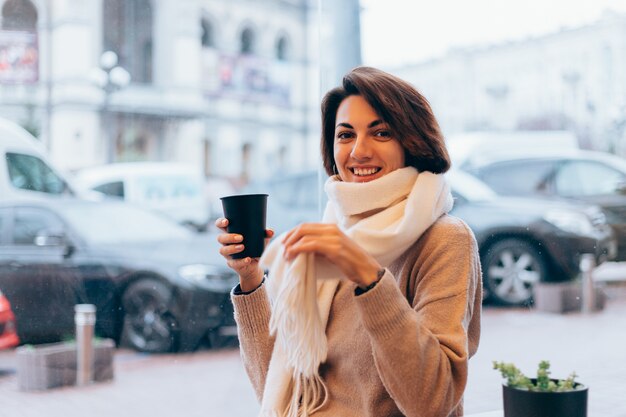 Una niña en un acogedor café se calienta con una taza de café caliente.