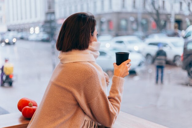 Una niña en un acogedor café se calienta con una taza de café caliente.