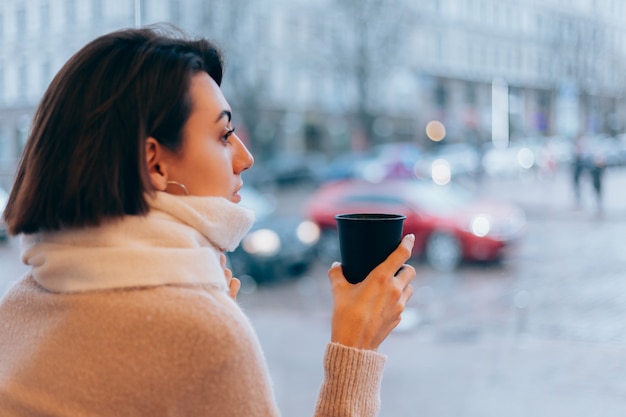 Una niña en un acogedor café se calienta con una taza de café caliente.