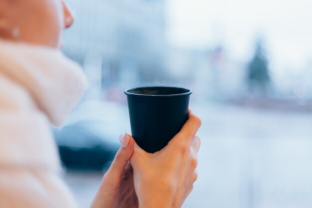 Una niña en un acogedor café se calienta con una taza de café caliente.