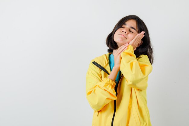 Niña acolchando la cara en sus manos en camisa, chaqueta y mirando soñolienta, vista frontal.