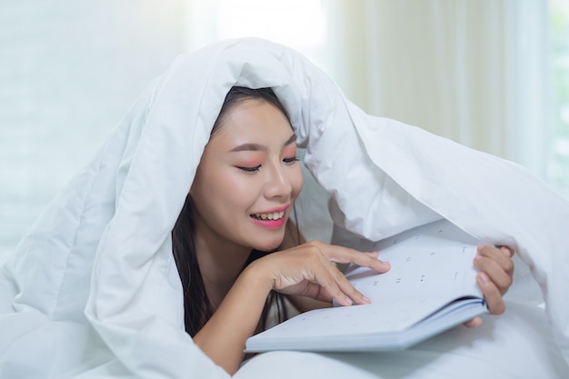 La niña acostada en la cama escuchando música y leyendo libros.