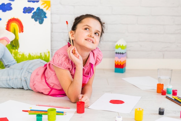 Niña acostada en el piso mirando hacia arriba mientras pinta sobre papel