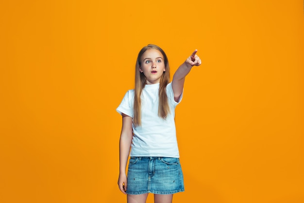 La niña adolescente feliz apuntando a usted, retrato de detalle de media longitud en espacio naranja.